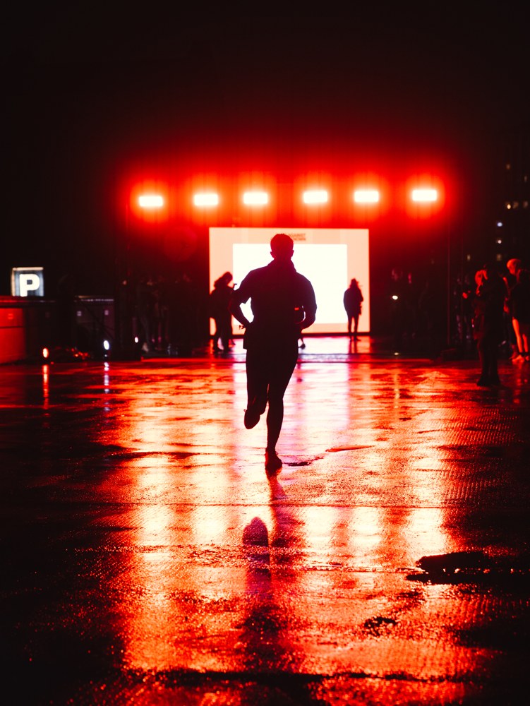 Runner silhouetted against red lights on wet pavement