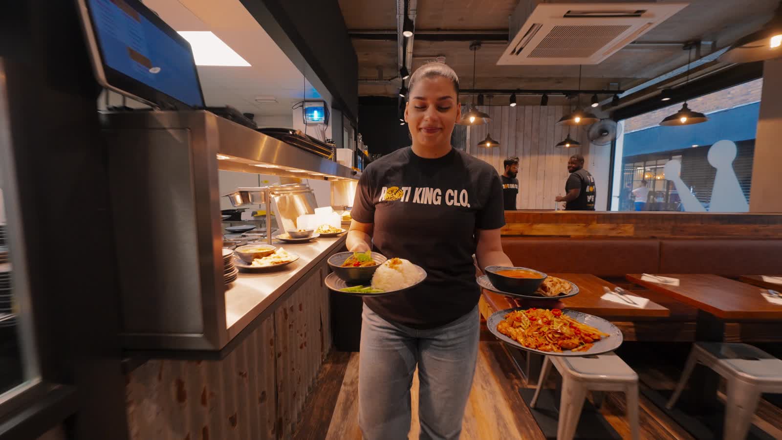 A Roti King team member serving dishes in the restaurant
